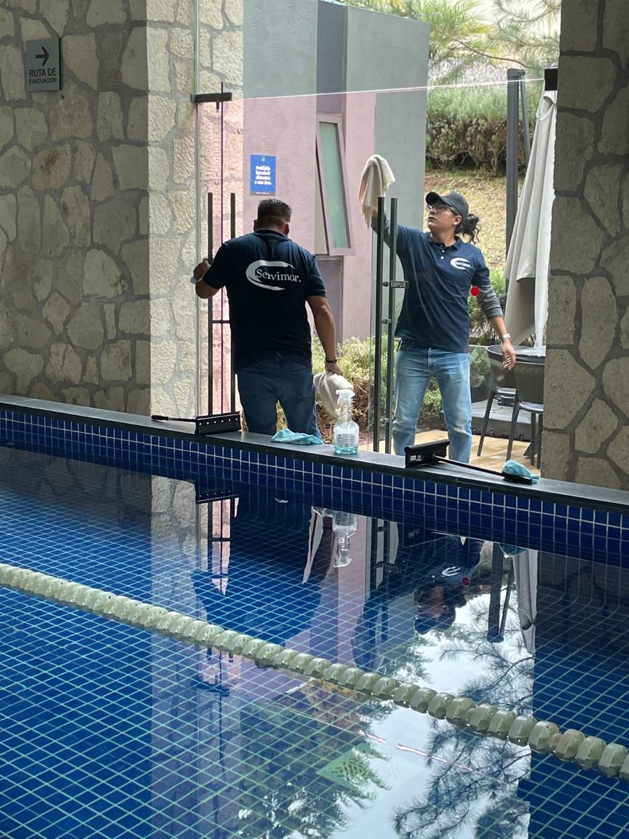 Equipo SERVIMOR limpiando cristales junto a una alberca